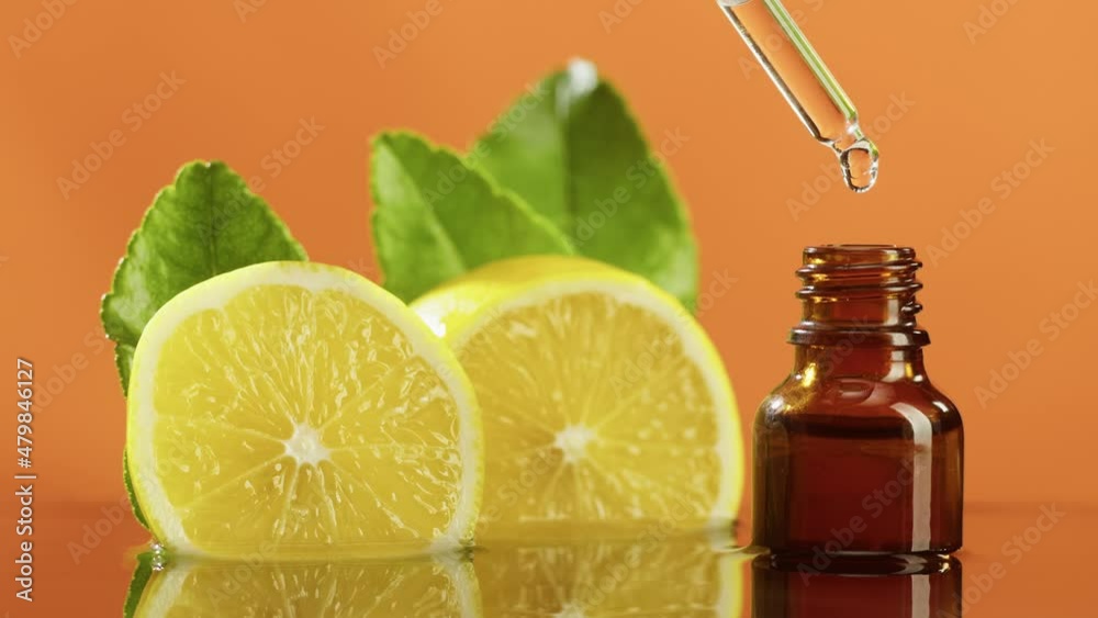 Dripping lemon juice from pipette into bottle close-up, vitamin oil. Making aroma serum on orange background. Dropping liquid citrus extract, skincare routine, treatment spa. Traditional medicine. Dripping lemon juice from pipette into bottle close-up, vitamin oil. Making aroma serum on orange background. Dropping liquid citrus extract, skincare routine, treatment spa. Traditional medicine.