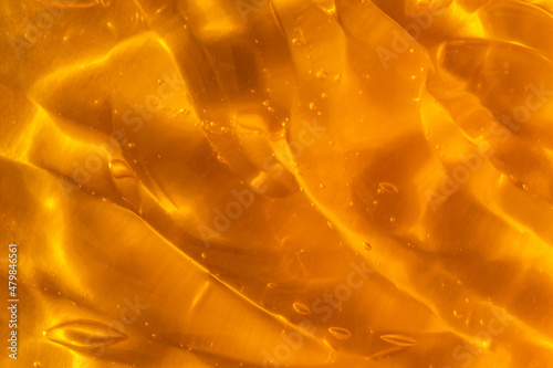 Texture of transparent yellow gel with air bubbles and waves on orange background. Concept of skin moisturizing, body care and prevention of covid19. Liquid beauty product closeup. Backdrop, flat lay
