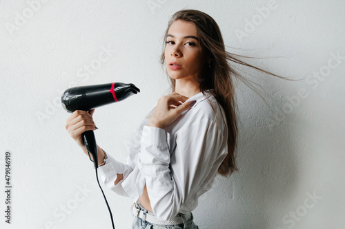 Attractive young woman drying her straight long brunette hair on white background. Woman is getting ready for work