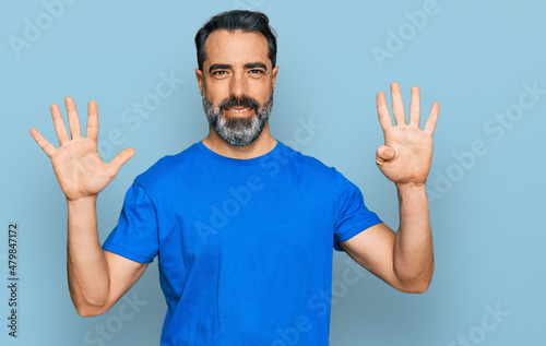 Middle aged man with beard wearing casual blue t shirt showing and pointing up with fingers number nine while smiling confident and happy. © Krakenimages.com