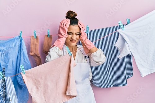 Beautiful brunette young woman washing clothes at clothesline suffering from headache desperate and stressed because pain and migraine. hands on head.