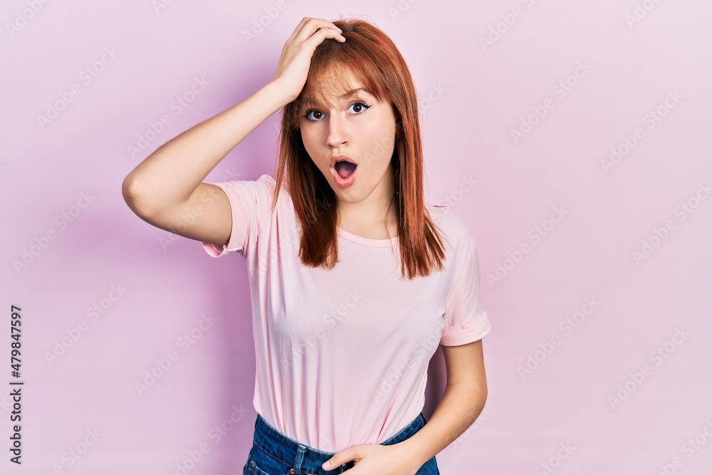 Redhead young woman wearing casual pink t shirt surprised with hand on head for mistake, remember error. forgot, bad memory concept. Redhead young woman wearing casual pink t shirt surprised with hand on head for mistake, remember error. forgot, bad memory concept.
