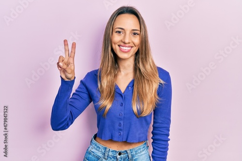 Beautiful hispanic woman wearing casual blue shirt showing and pointing up with fingers number two while smiling confident and happy.