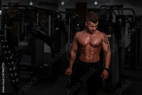 Handsome man model bodybuilder trainer with sexy naked torso in the gym. Sportsman doing workout