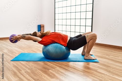 Young redhead man training using fit ball at sport center