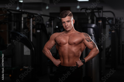 Strong handsome fitness model man with a sports body and tattoo on hand does a workout in the gym