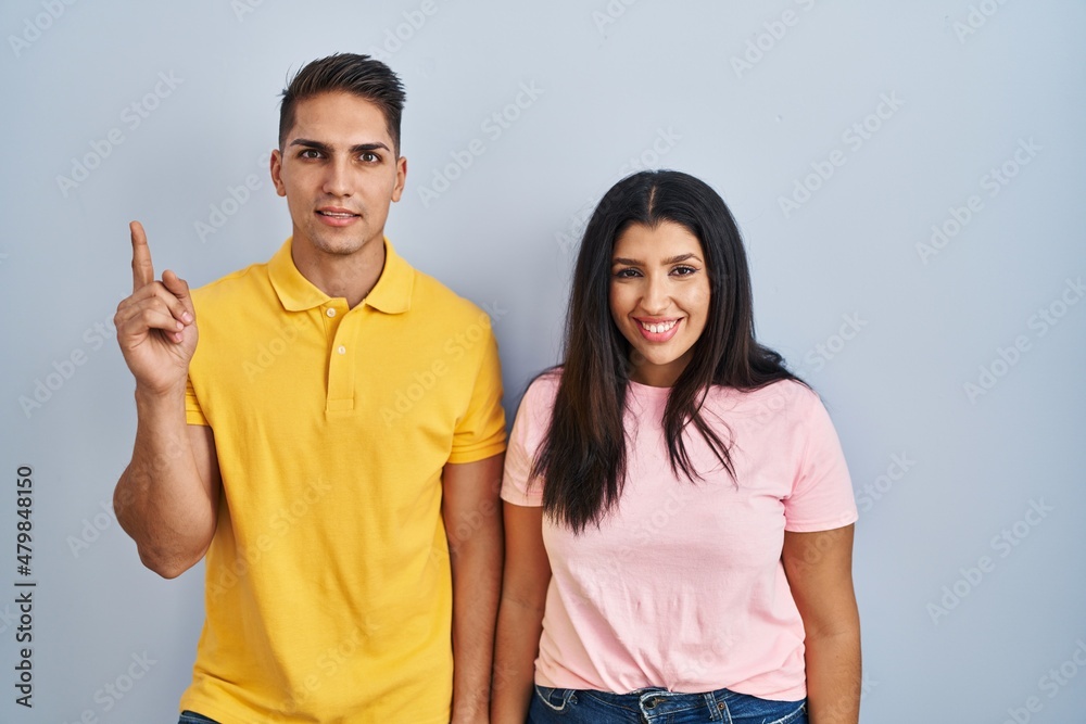 Young couple standing over isolated background showing and pointing up with finger number one while smiling confident and happy. Young couple standing over isolated background showing and pointing up with finger number one while smiling confident and happy.