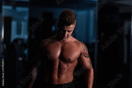 Muscular bodybuilder guy standing on gym in the dark