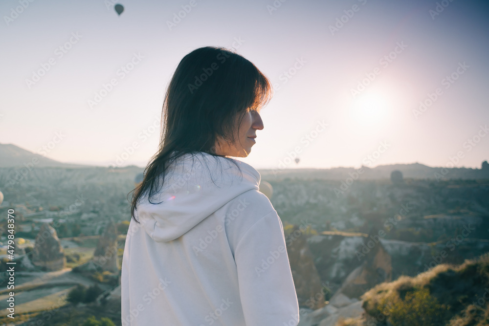 Woman watching the sunrise and hot air balloons taking off over valley in Cappadocia, Goreme, Turkey Woman watching the sunrise and hot air balloons taking off over valley in Cappadocia, Goreme, Turkey