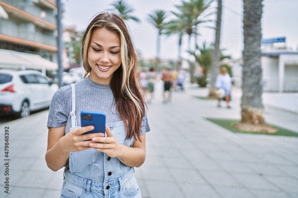 Fototapeta premium Young caucasian girl smiling happy using smartphone at the city.