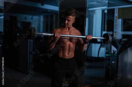 Sporty strong man with hairstyle with muscular body doing exercise in the gym on a dark blue background