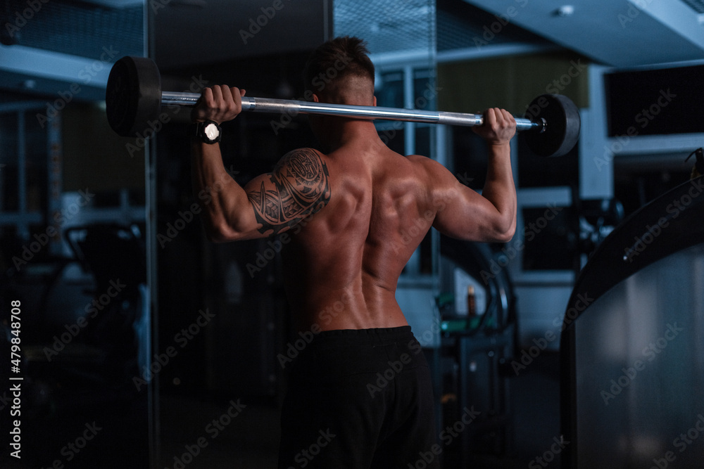 Athletic strong bodybuilder man with bare back and muscles doing exercise in the gym at night Athletic strong bodybuilder man with bare back and muscles doing exercise in the gym at night