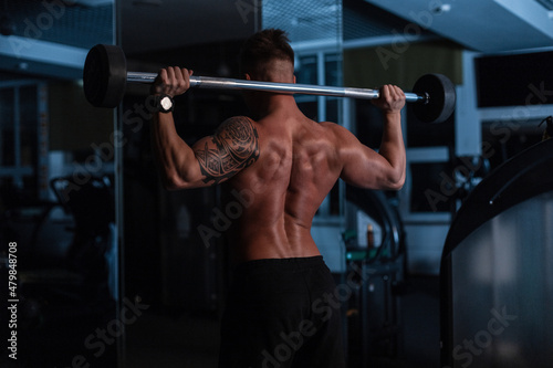 Athletic strong bodybuilder man with bare back and muscles doing exercise in the gym at night