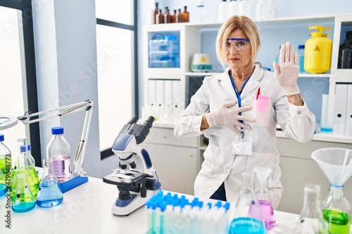 Middle age blonde woman working at scientist laboratory swearing with hand on chest and open palm  making a loyalty promise oath