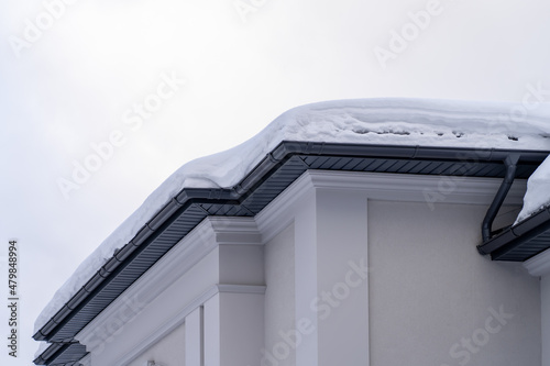 Fotografie, Obraz Corner of house with new roof made of gray metal tiles and gutter covered with thick layer of snow in winter