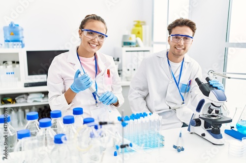 Man and woman wearing scientist uniform using pipette and microscope working at laboratory