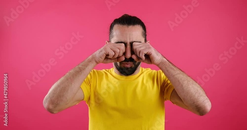 Shocked man rubbing his eyes in disbelief over pink background