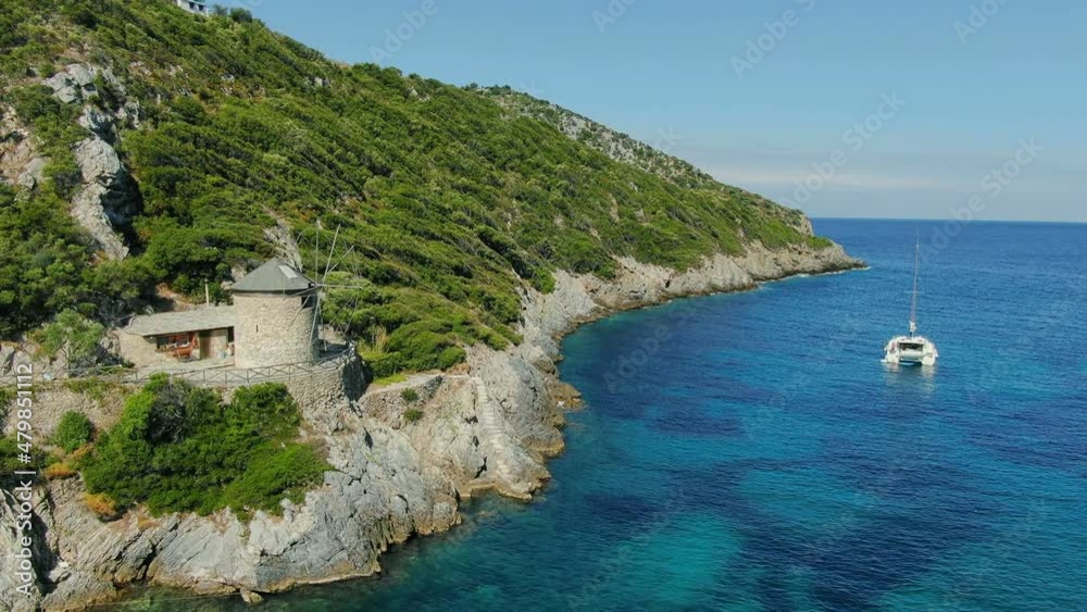 Aerial view of the Greek sea coast with a beach. Traditional windmill built on the rock right next to the shore on the first line. Aerial view of the Greek sea coast with a beach. Traditional windmill built on the rock right next to the shore on the first line.