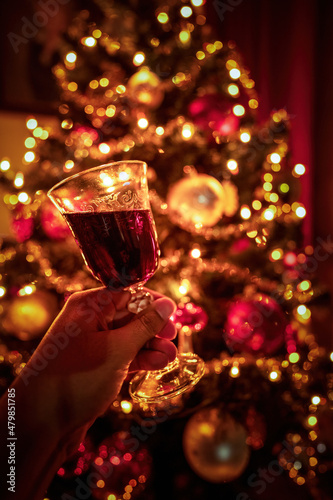 Obraz na płótnie Hand cheering with tilted red wine glass against out of focus christmas tree lights, xmas festive celebration concept. w salonie