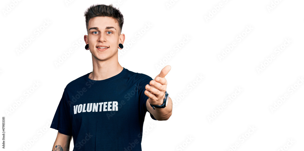 Young caucasian boy with ears dilation wearing volunteer t shirt smiling friendly offering handshake as greeting and welcoming. successful business. Young caucasian boy with ears dilation wearing volunteer t shirt smiling friendly offering handshake as greeting and welcoming. successful business.