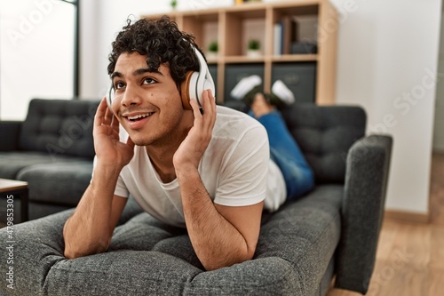 Young hispanic man listening to music lying on the sofa at home.
