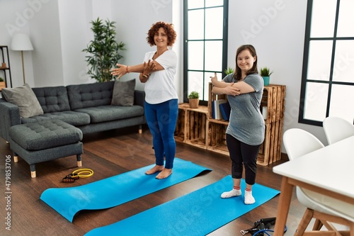 Mature mother and down syndrome daughter doing exercise at home. Stretching at the living room