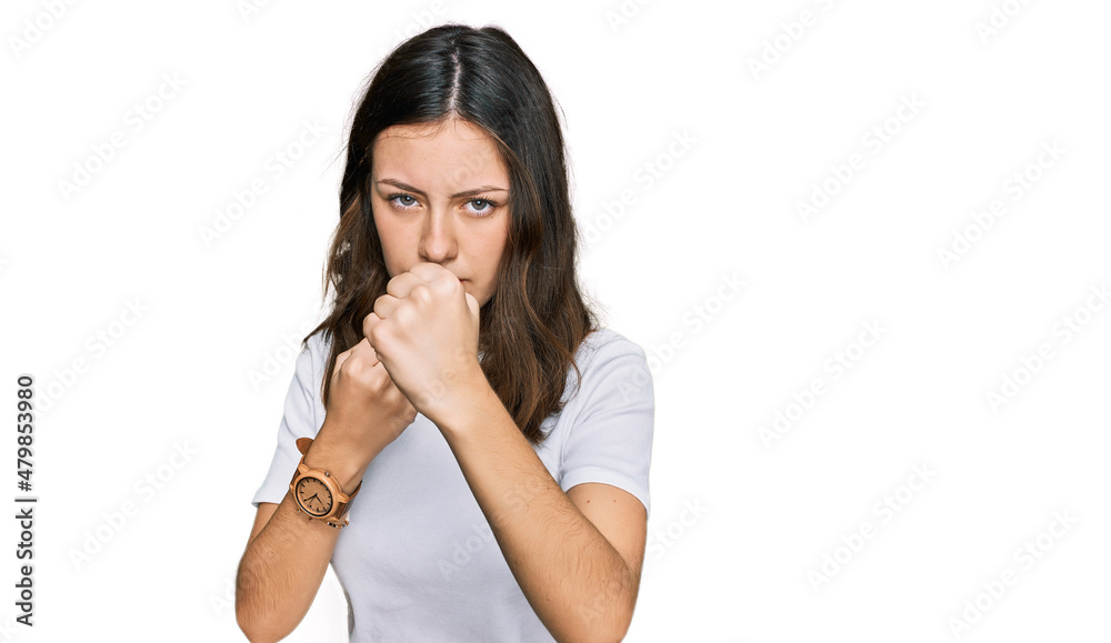 Young beautiful woman wearing casual white t shirt ready to fight with fist defense gesture, angry and upset face, afraid of problem Young beautiful woman wearing casual white t shirt ready to fight with fist defense gesture, angry and upset face, afraid of problem