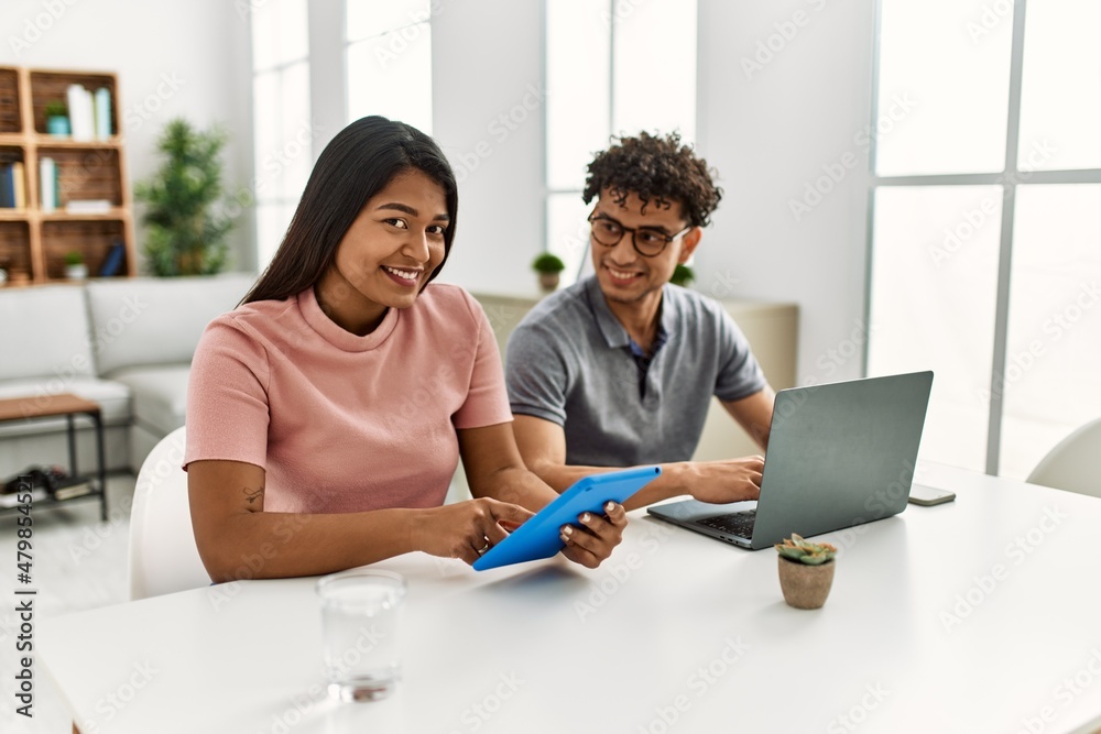 Young latin couple working using laptop and touchpad sitting on the table at home. Young latin couple working using laptop and touchpad sitting on the table at home.