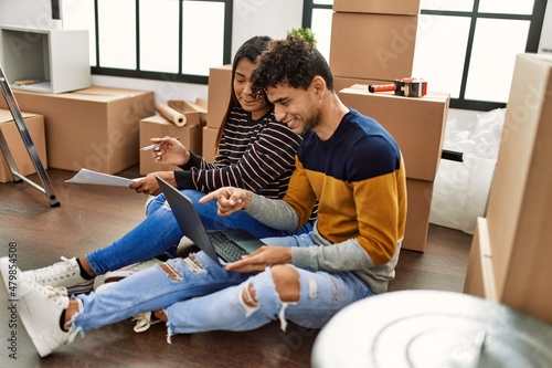 Young latin couple using laptop sitting on the floor at new home.