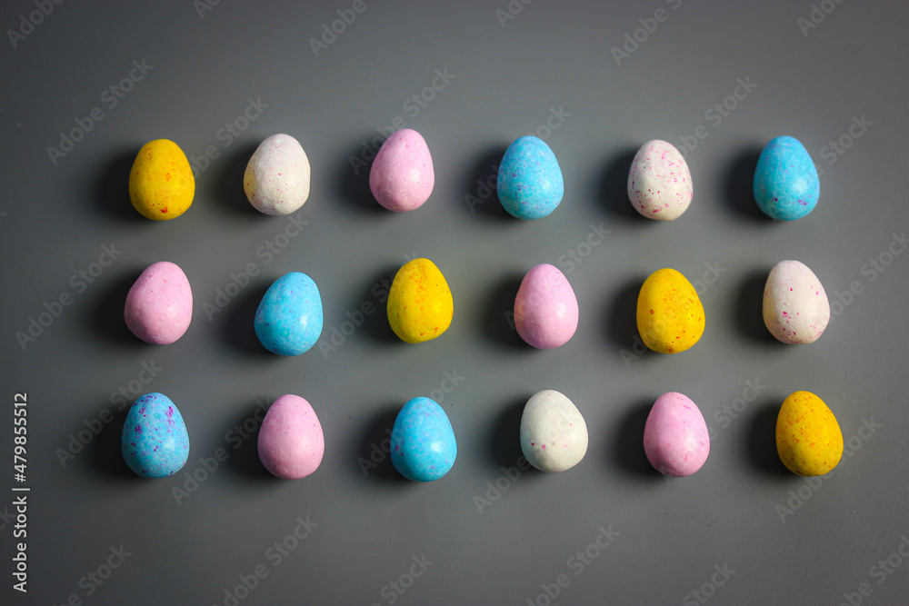 Multicolored bright Easter chocolate eggs yellow, white, pink, blue colors scattered on dark table background top view. Sweets, treats for children, kids in spring season holiday. Minimal Easter idea.
