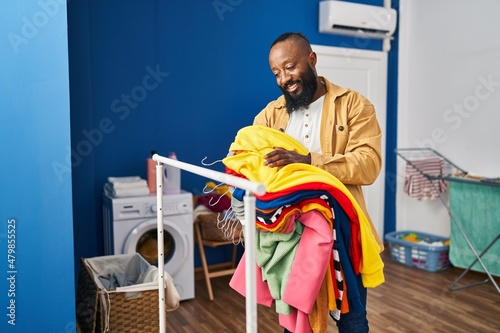Young african american man smiling confident holding clothes at laundry room