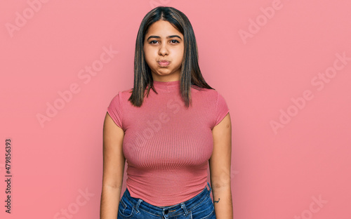 Young hispanic girl wearing casual t shirt puffing cheeks with funny face. mouth inflated with air, crazy expression. photo