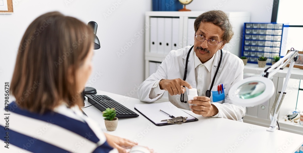 Fototapeta premium Middle age man and woman wearing doctor uniform having medical consultation holding pills at clinic
