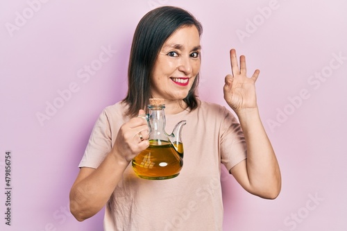 Canvastavla Middle age hispanic woman holding olive oil can doing ok sign with fingers, smil