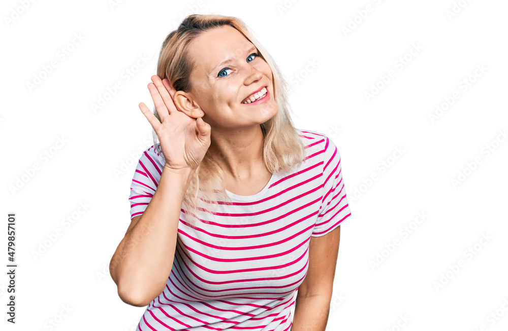 Young caucasian woman wearing casual clothes smiling with hand over ear listening an hearing to rumor or gossip. deafness concept. Young caucasian woman wearing casual clothes smiling with hand over ear listening an hearing to rumor or gossip. deafness concept.