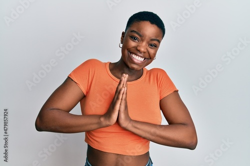 Young african american woman wearing casual orange t shirt praying with hands together asking for forgiveness smiling confident.