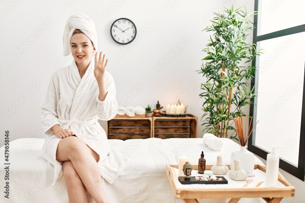 Young blonde woman wearing bathrobe at wellbeing spa showing and pointing up with fingers number four while smiling confident and happy. Young blonde woman wearing bathrobe at wellbeing spa showing and pointing up with fingers number four while smiling confident and happy.