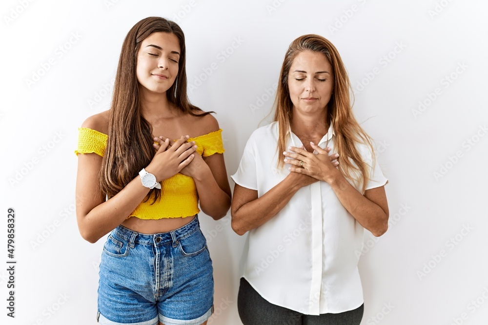 Mother and daughter together standing together over isolated background smiling with hands on chest with closed eyes and grateful gesture on face. health concept. Mother and daughter together standing together over isolated background smiling with hands on chest with closed eyes and grateful gesture on face. health concept.