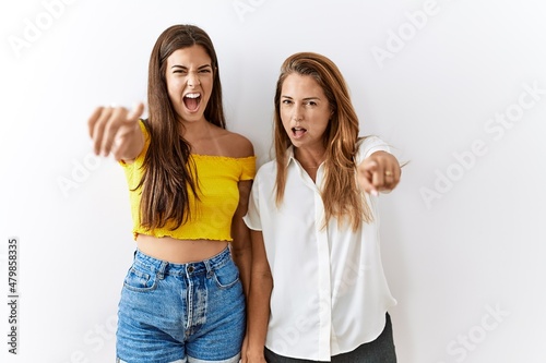 Mother and daughter together standing together over isolated background pointing displeased and frustrated to the camera, angry and furious with you