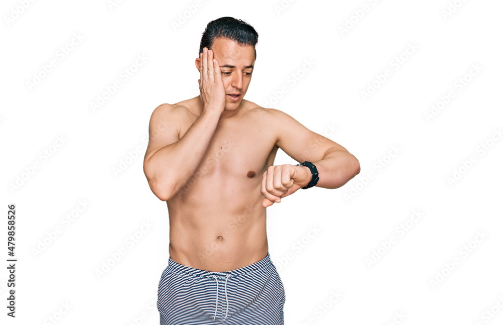 Handsome young man wearing swimwear shirtless looking at the watch time worried, afraid of getting late Handsome young man wearing swimwear shirtless looking at the watch time worried, afraid of getting late