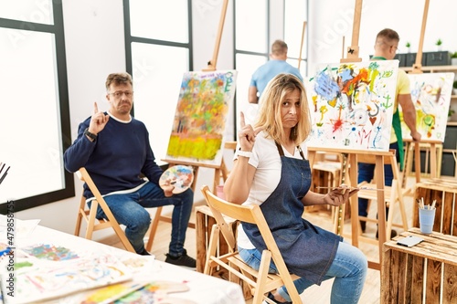 Group of middle age artist at art studio pointing up looking sad and upset  indicating direction with fingers  unhappy and depressed.