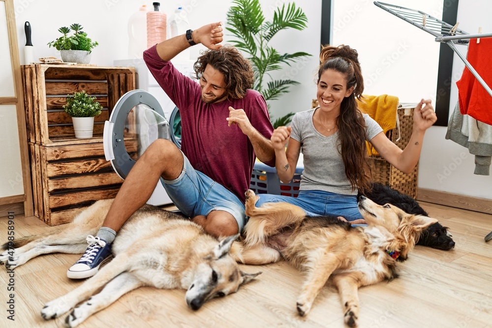 Young hispanic couple doing laundry with dogs dancing happy and cheerful, smiling moving casual and confident listening to music