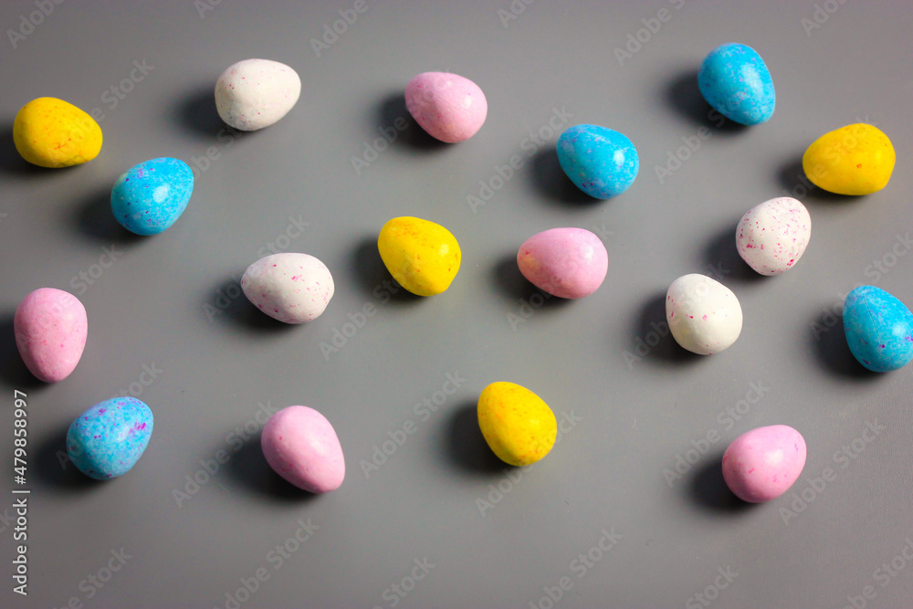 Multicolored bright Easter chocolate eggs yellow, white, pink, blue colors scattered on dark table background top view. Sweets, treats for children, kids in spring season holiday. Minimal Easter idea. Multicolored bright Easter chocolate eggs yellow, white, pink, blue colors scattered on dark table background top view. Sweets, treats for children, kids in spring season holiday. Minimal Easter idea.