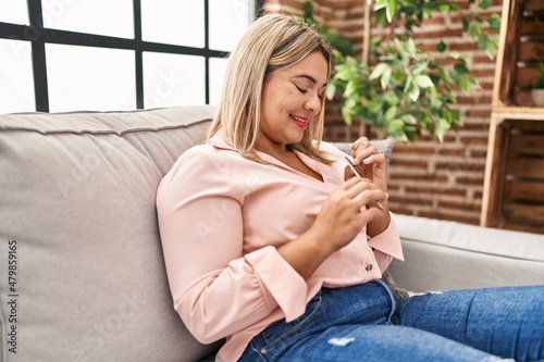 Young hispanic woman using nails lime sitting on sofa at home