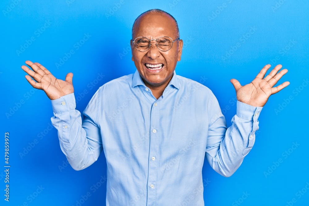 Middle age latin man wearing casual clothes and glasses celebrating mad and crazy for success with arms raised and closed eyes screaming excited. winner concept Middle age latin man wearing casual clothes and glasses celebrating mad and crazy for success with arms raised and closed eyes screaming excited. winner concept