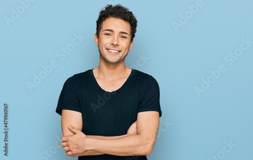 Fotótapéta Young handsome man wearing casual black t shirt happy face smiling with crossed arms looking at the camera