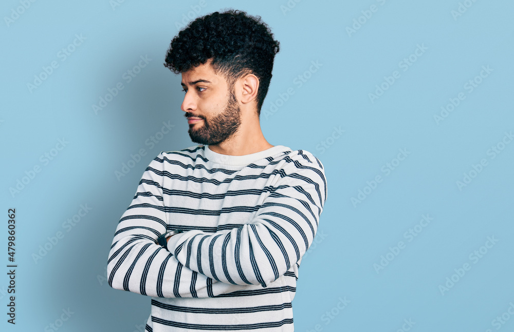 Obraz premium Young arab man with beard wearing casual striped sweater looking to the side with arms crossed convinced and confident
