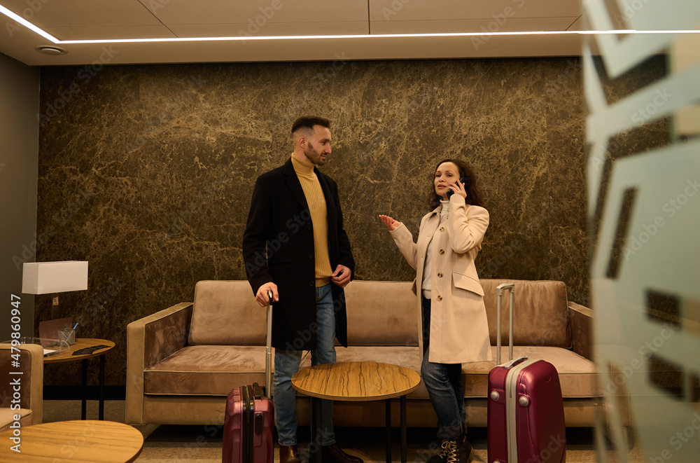Beautiful newlywed couple in the VIP room of the airport terminal. Handsome business man looking at his female partner talking on the phone, negotiating and booking hotel waiting to board the flight. Beautiful newlywed couple in the VIP room of the airport terminal. Handsome business man looking at his female partner talking on the phone, negotiating and booking hotel waiting to board the flight.