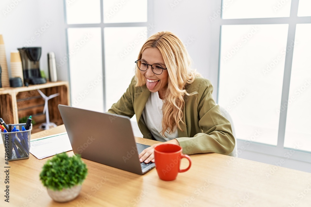 Beautiful blonde woman working at the office with laptop sticking tongue out happy with funny expression. emotion concept. Beautiful blonde woman working at the office with laptop sticking tongue out happy with funny expression. emotion concept.