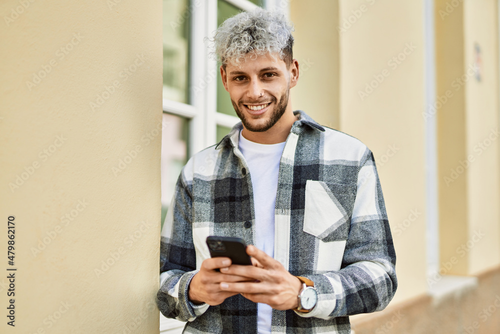 Fototapeta premium Young hispanic man smiling happy using smartphone at the city.